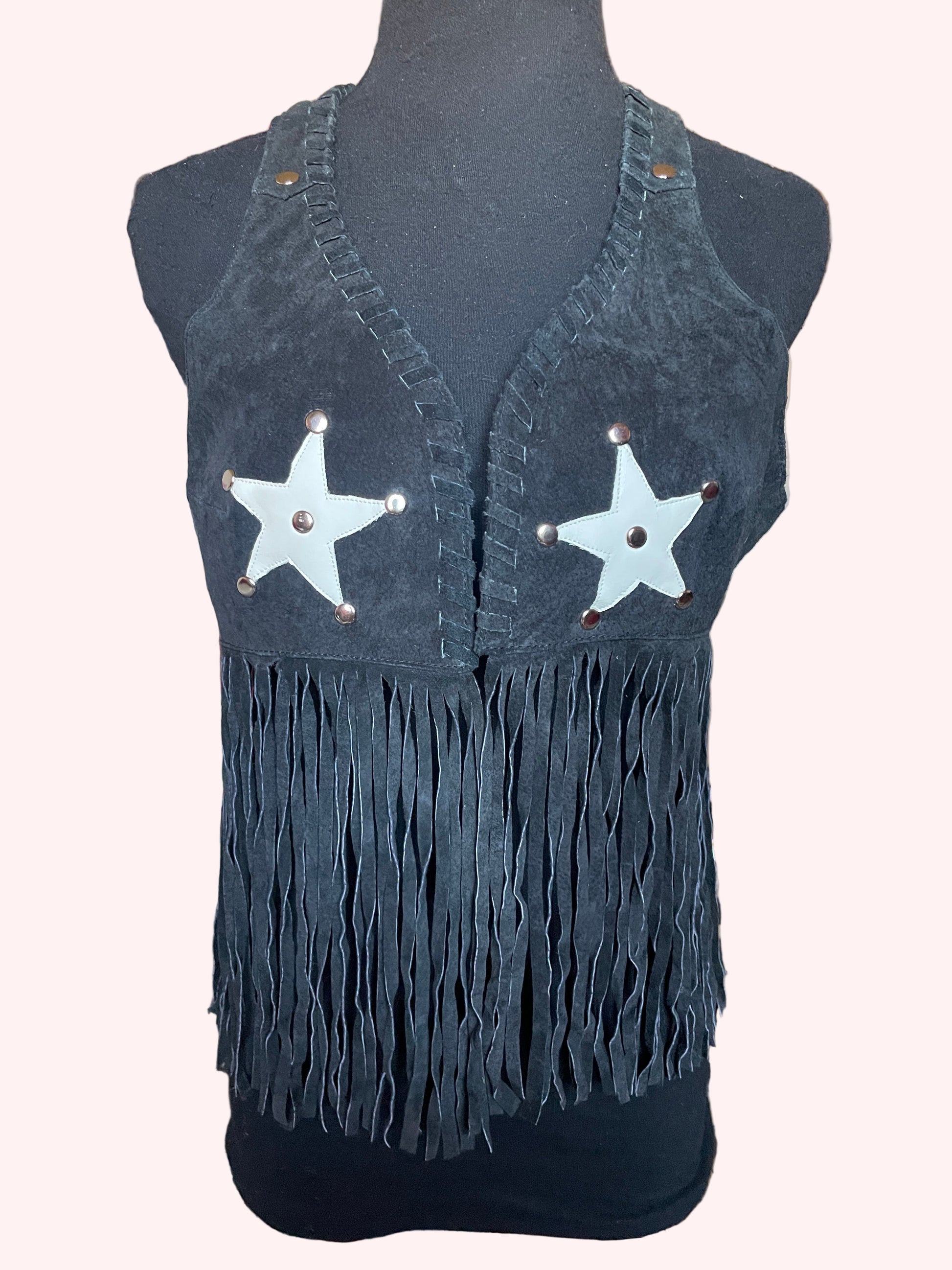 Black leather vest with fringe and white star patches on a blurred indoor background